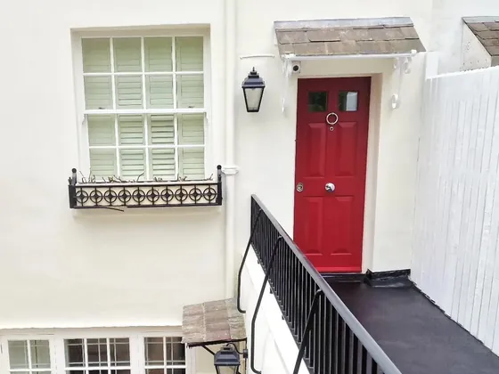 White painted house with a red front door, a sash window and black railings