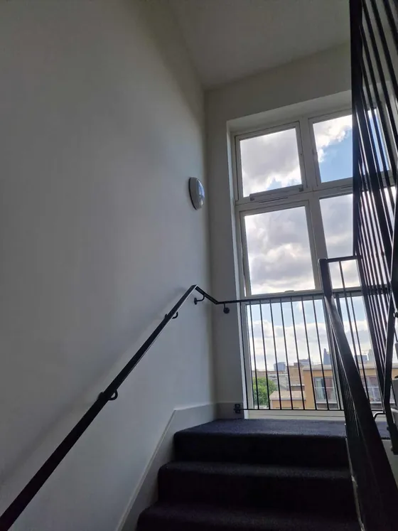 Stairwell with pale walls, a black handrail and a tall window