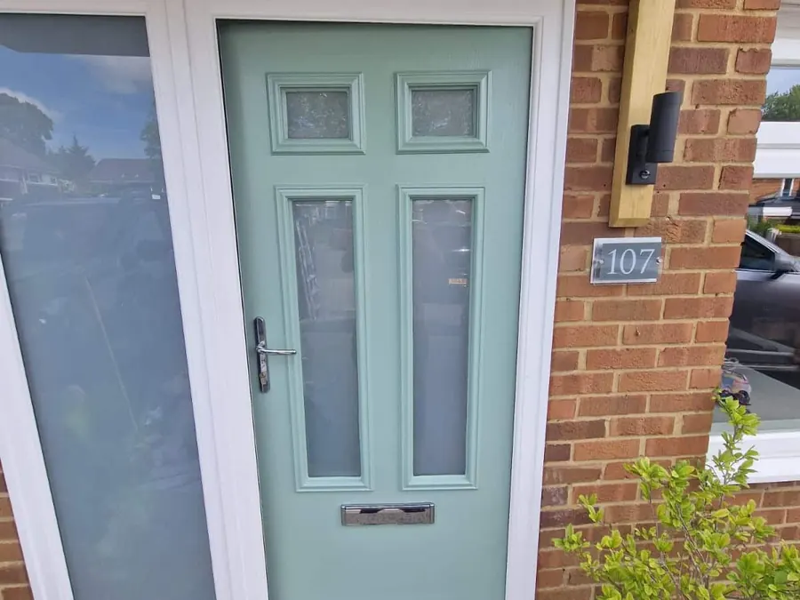A sage green front door with a white frame on a brick house